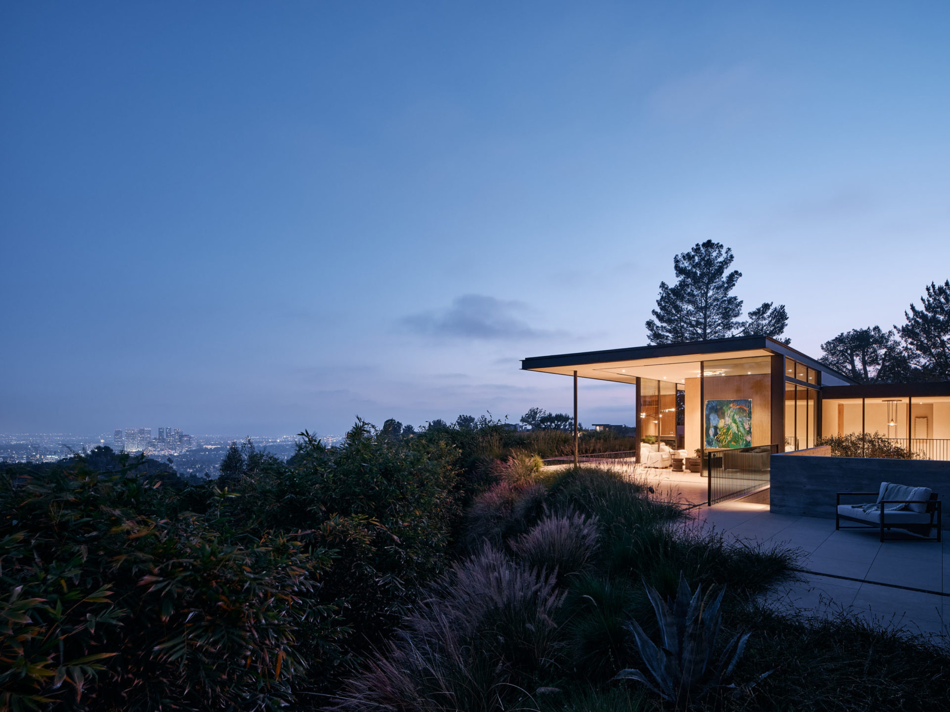 Modern hillside residence at blue hour with floor-to-ceiling glass walls overlooking city lights