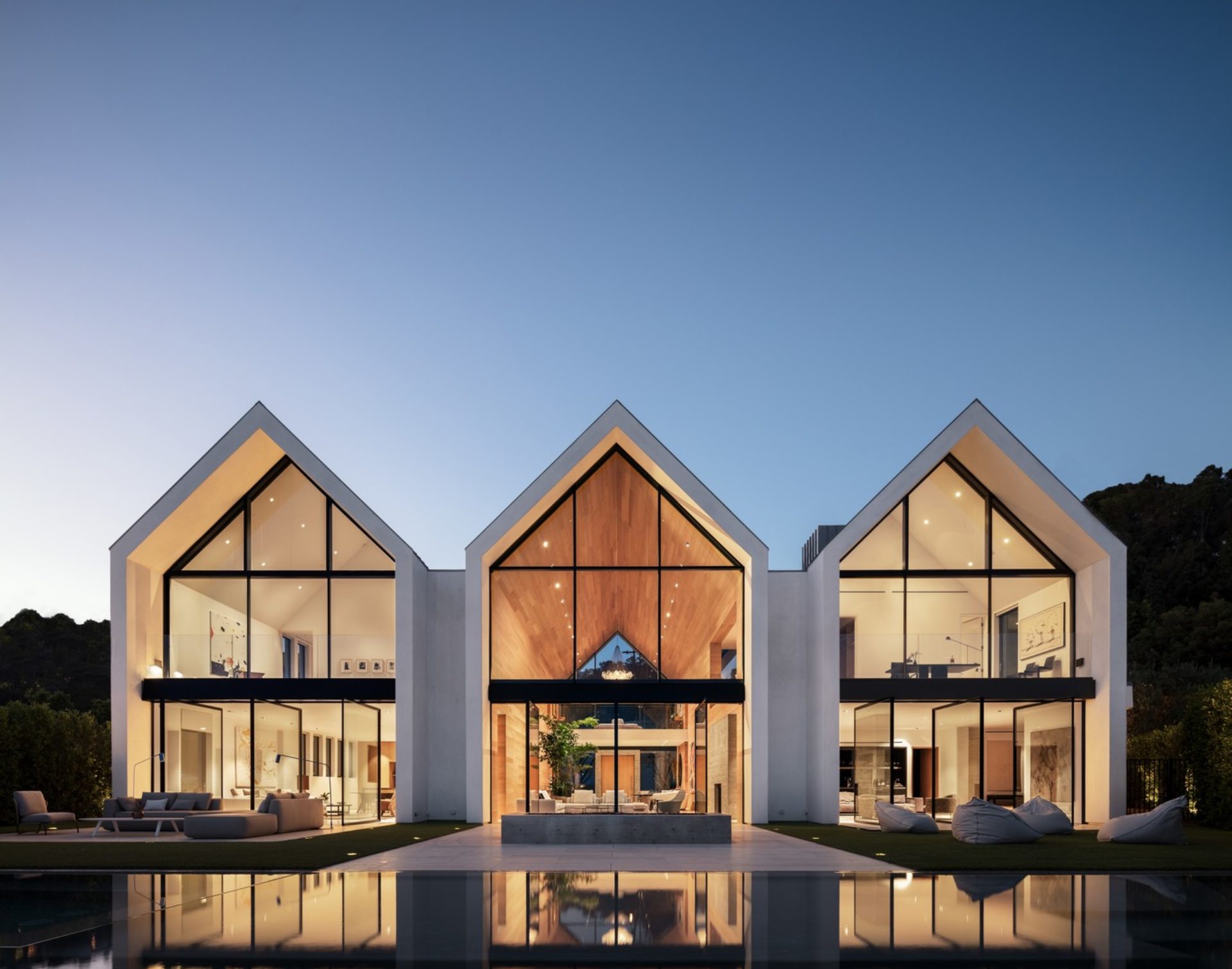 Modern gabled home with three pavilions featuring Styline minimal frame floor-to-ceiling glass walls reflected in pool at twilight
