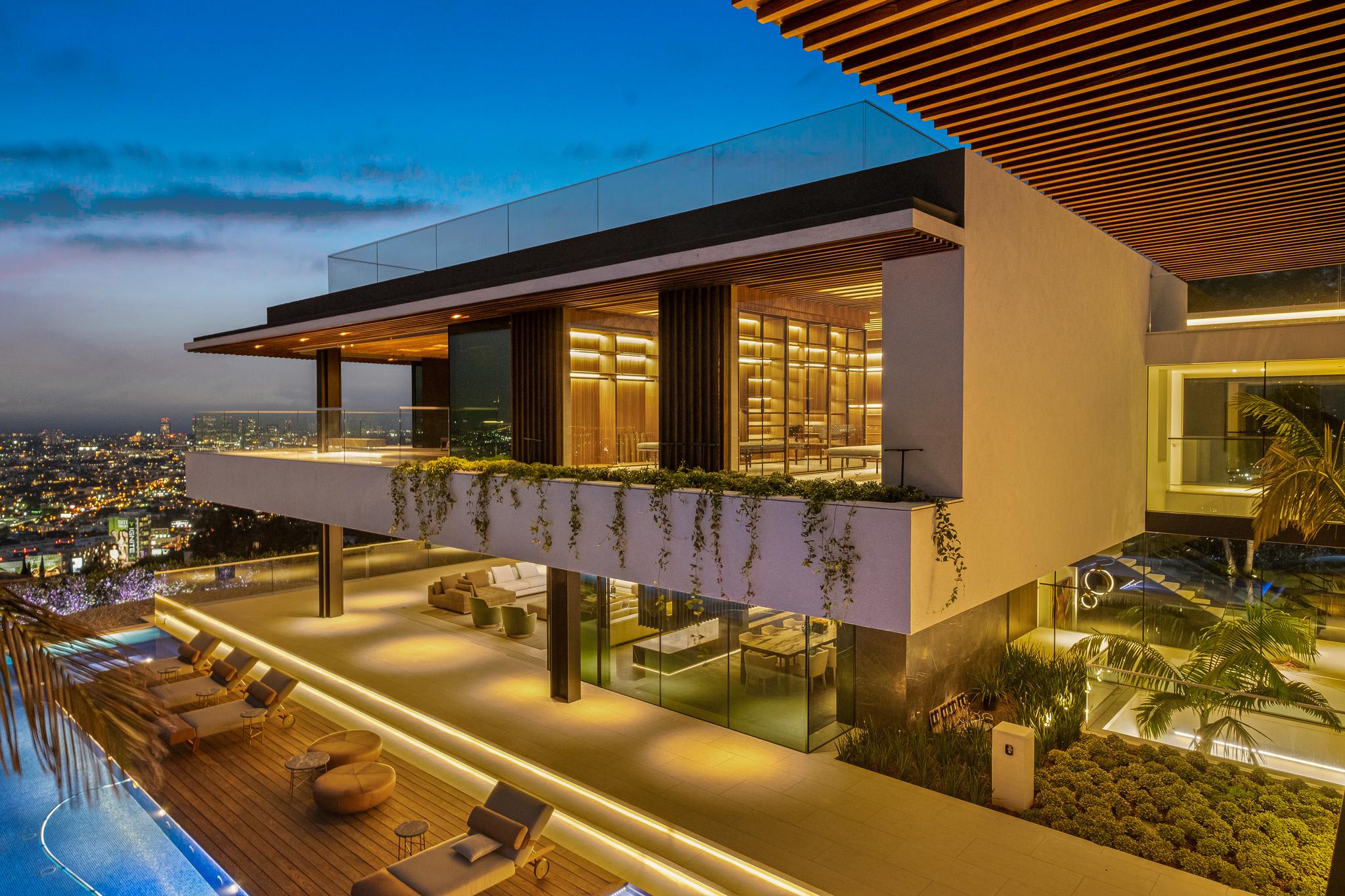 Hillside luxury residence at blue hour with floor-to-ceiling Styline sliding glass walls, pool deck, and city views
