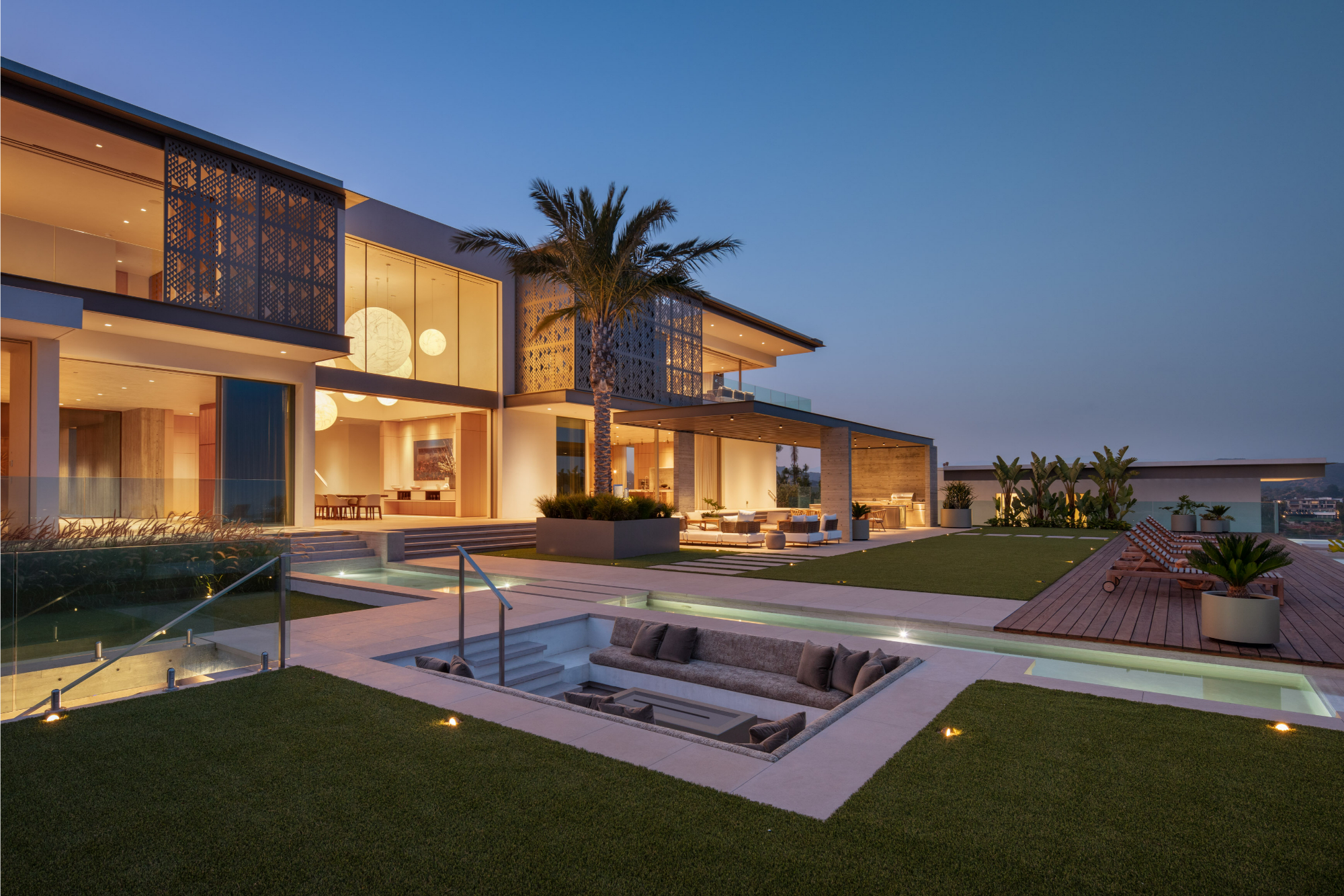 Luxury home at twilight with warm interior glow through floor-to-ceiling Styline glass walls and infinity pool