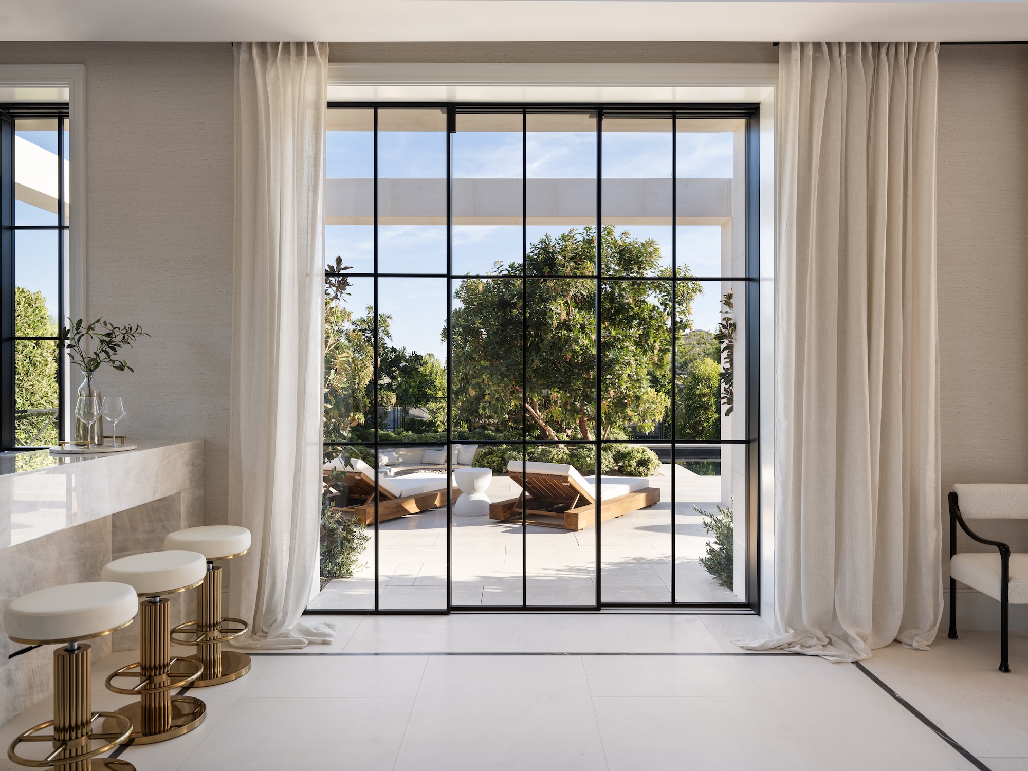 Steel Essence™ steel-look floor-to-ceiling windows with grid pattern looking out to poolside terrace with lounge chairs