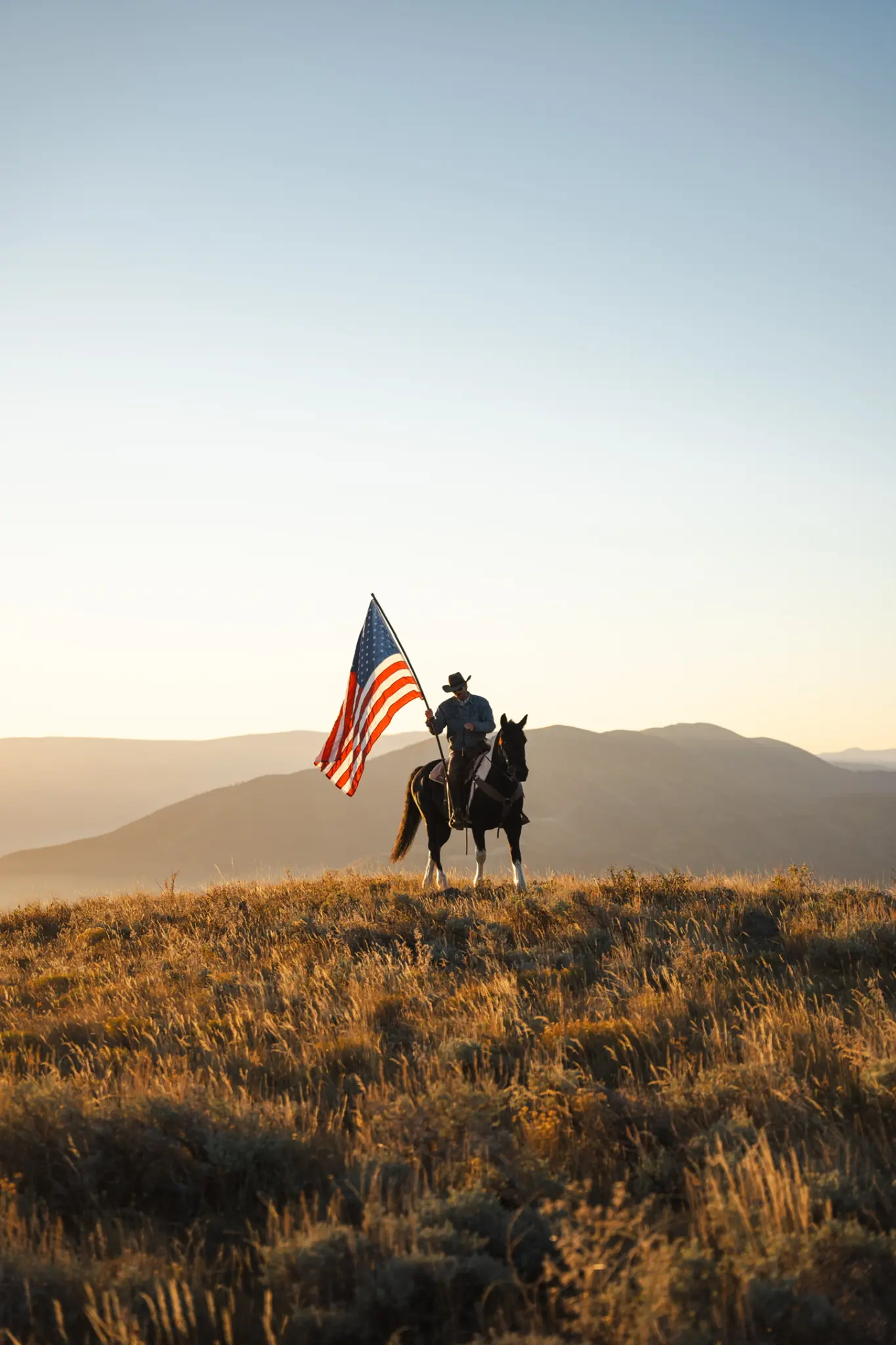 Cowboy on horseback carrying the American flag at golden hour on open rangeland